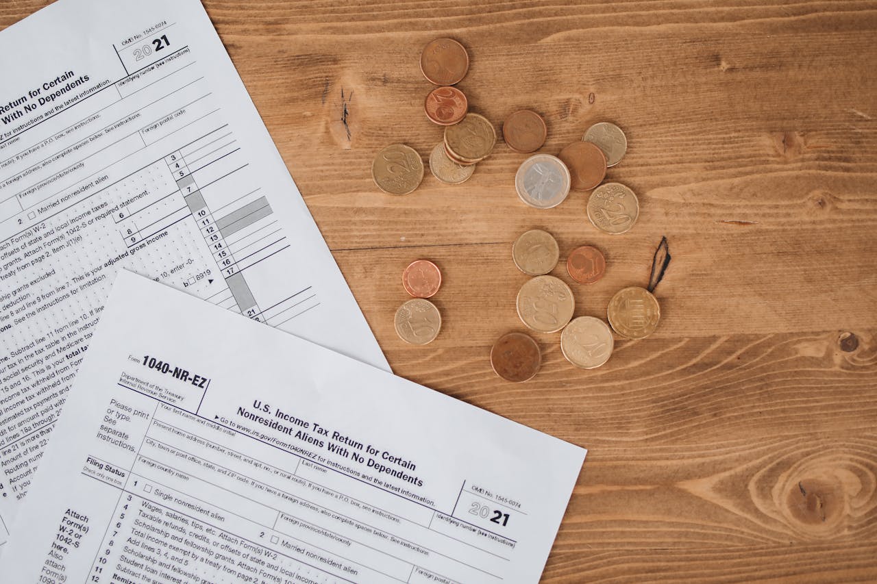 hero-img-01 Flat lay of tax forms and scattered coins on a wooden table, illustrating finance and taxation concepts.