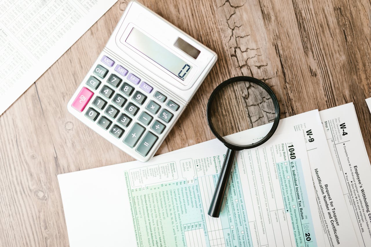 about-01 Tax forms laid out with a calculator and magnifying glass on a wooden surface, perfect for finance themes.